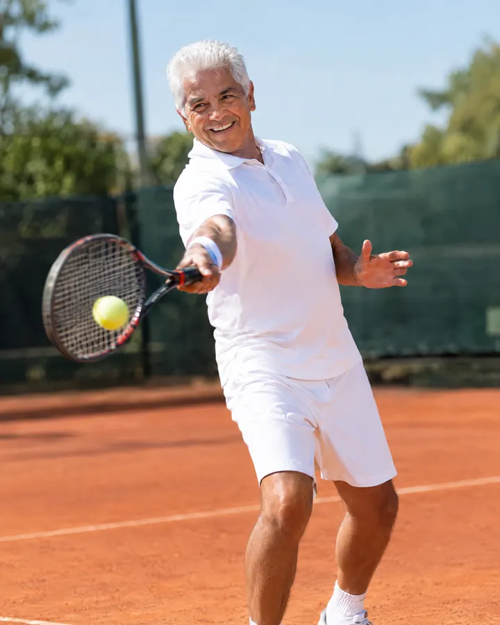 Un hombre mayor juega tenis en una cancha de arcilla.